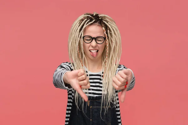 Young girl with dreadlocks in a striped shirt and jeans jumpsuit is upset holding thumbs down. — 스톡 사진