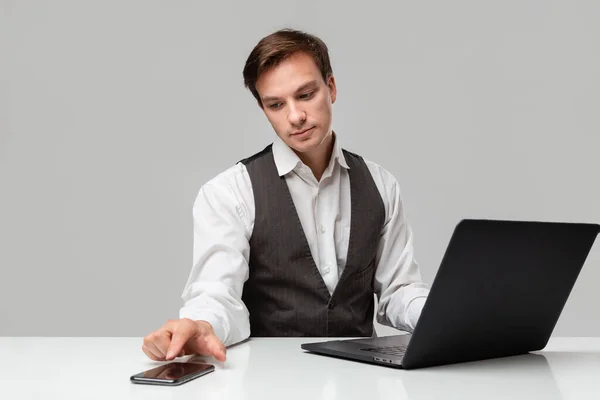 Empresario con camiseta blanca y chaleco gris trabajando en un portátil. Hombre mirando a la cámara — Foto de Stock