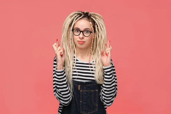 Young girl with long dreads standing over pink background holding fingers crossed for good luck — ストック写真