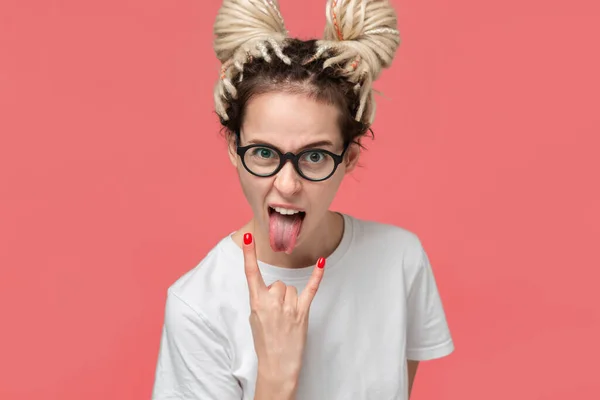 Young girl with dreads in a white shirt and glasses showing gesture of rock music sticking tongue — ストック写真