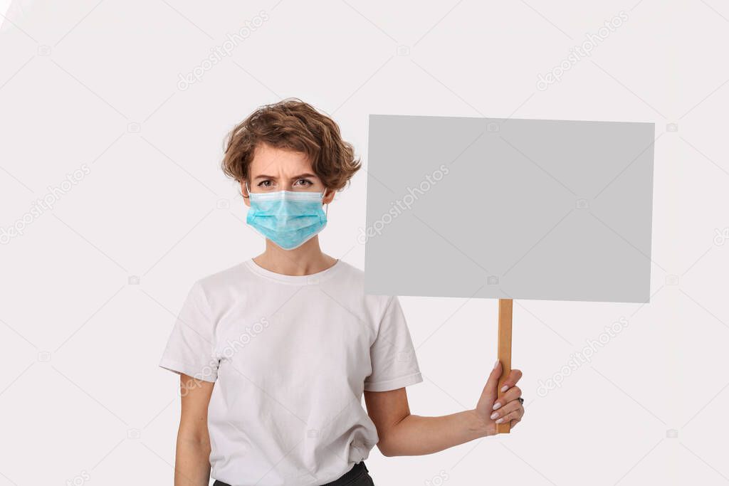 Worried woman wearing blue medical mask holds picket sign with copy space and piniting at her head