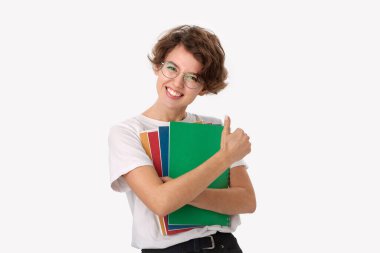 Beyaz gömlekli, gözlüklü renkli klasörler tutan ve baş parmağını gösteren heyecanlı bir genç.