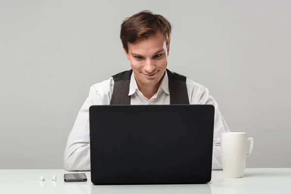 Homem pensando sentado em uma mesa branca com laptop, smartphone e xícara de café — Fotografia de Stock