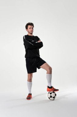Siyah spor giyimli kendine güvenen bir futbolcu el ele tutuşmuş ve kameraya bakan bir topa basıyor. Futbol kupası elemeleri için antrenman.