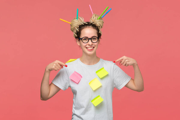 Smiling student in a white shirt and glasses, sticky notes on a shirt and colorful markers in dreads pointing with fingers at herself. Concept of creative thinking