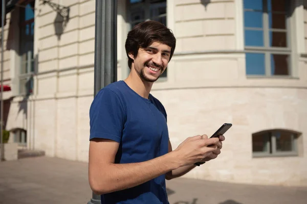 髭と口ひげを生やした若いブルネットの男は 携帯電話で通りを歩いて話して笑っている コミュニケーションの概念 ロイヤリティフリーのストック画像