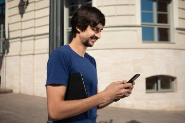 Sakallı ve bıyıklı genç esmer adam caddede yürüyen cep telefonunun ekranına bakıp gülümsüyor. İletişim kavramı