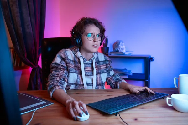 困惑的女孩坐在舒适的椅子上 看着电脑屏幕 房间里的霓虹灯 在网上焦虑地阅读新闻 在家工作 自我隔离和隔离 — 图库照片