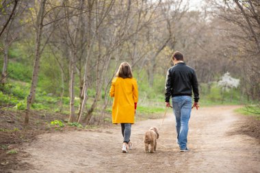 Genç bir çift ormanda bir köpekle yürüyor. Sarı ceketli genç bir kadın kameraya bakıyor. Mutlu aile