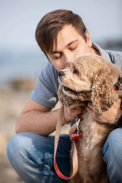 Young man hugging a dog at the sea shore. The man petting obedient dog on a sea coast. Best friends. Dog walking outdoors