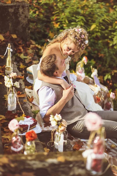 Les mariés dans un style rustique assis sur des marches de pierre à la forêt d'automne ensoleillée, entouré d'un décor de mariage . — Photo