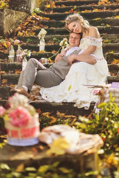Les mariés dans un style rustique assis sur des marches de pierre à la forêt d'automne ensoleillée, entouré d'un décor de mariage . — Photo