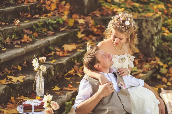 Les mariés dans un style rustique étreignant assis sur des marches de pierre à la forêt d'automne, entouré d'un décor de mariage . — Photo