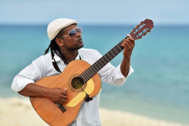 Yaz günü gitar Karayip deniz kenarında oynarken Afro-Amerikan adam müzisyen