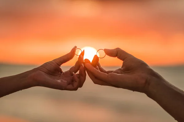 Silah düğün çift altın yüzük bir arka plan üzerinde günbatımında tutun