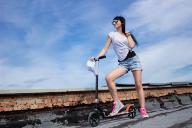Suglasses genç kadın tekme scooter bir çatı üzerinde yakın duruyor