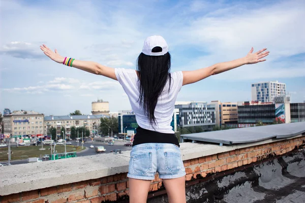 Mujer joven está de pie una espalda en un techo, levantando las manos y lo — Foto de Stock