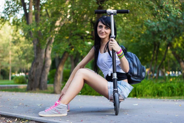 Beautiful young brunette woman is sitting on her kick scooter in — Stock Photo, Image