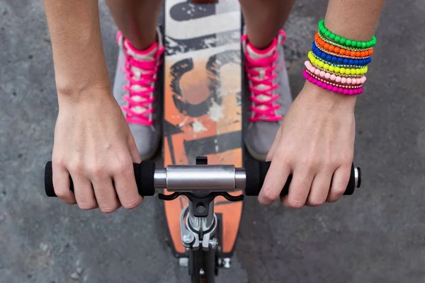 Atleta mujer joven con patada scooter está sosteniendo sus manos en la manija de la bicicleta. Piernas en el fondo — Foto de Stock