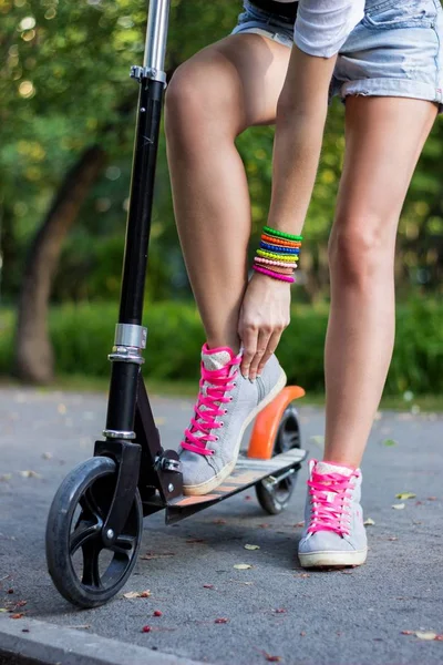 Bir tekme scooter üzerinde kadın binici fermuar, ayakkabılarını asfalt yol bir parkta, tespit etmek — Stok fotoğraf