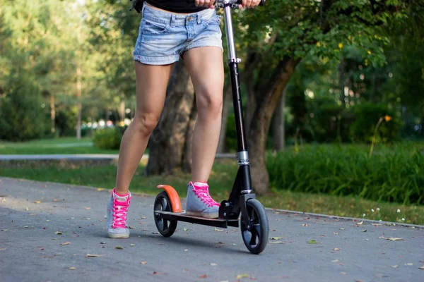 Female athlete rider is riding on a kick scooter in the park at summer sunny day — Stock Photo, Image