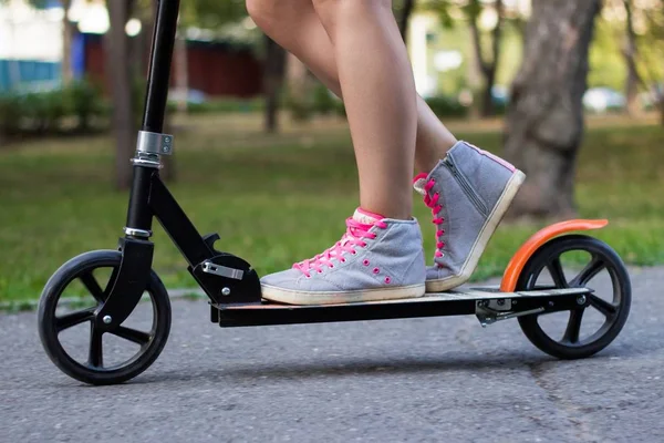 Mujer atleta adolescente está montando en una patada scooter en el parque en verano día soleado — Foto de Stock