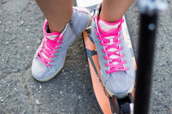Vista de cerca atleta joven con patinete scooter se coloca sus pies en zapatos grises con cordones rosados para montar en bicicleta sobre un fondo de asfalto — Foto de Stock