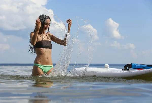 Jeune belle femme saupoudrer l'eau de la mer près de surf d — Photo