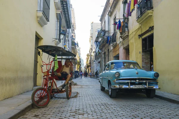Blue retro car and trishaws are parked on pavement in narrow str Stock Picture