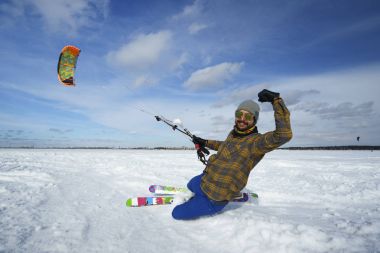 Happy sportsman in bright clothes skies with kite on winter snow clipart