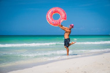 Happy handsome man in pink hat is standing with big inflatable r