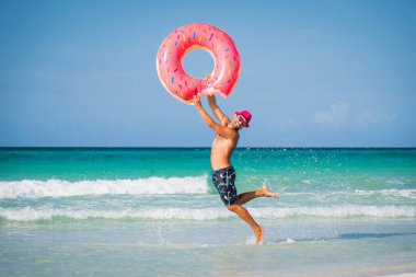 Pembe şapkalı mutlu yakışıklı adam büyük şişme tüp ile atlamak 