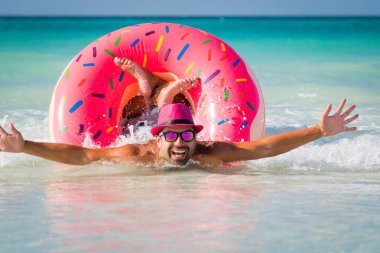 Pembe şapkalı mutlu yakışıklı komik adam büyük inflatab üzerinde yüzüyor