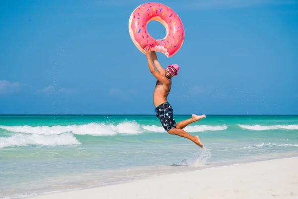 Homem bonito feliz no chapéu cor-de-rosa joga acima o tubo inflável grande sobre Imagem De Stock