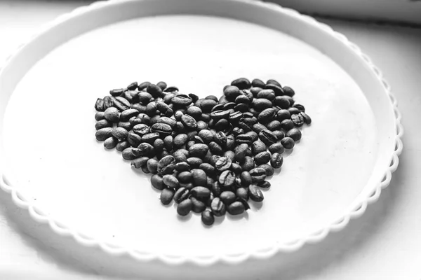 Granos de café en forma de corazón sobre fondo hermoso. Amor. Inscripción. En plato blanco . — Foto de Stock