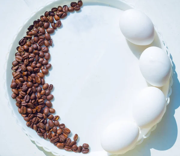 Grãos de café em forma de lua na placa branca com três ovos — Fotografia de Stock