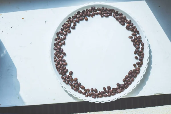 Kaffebönor i rund form på den vita plattan — Stockfoto