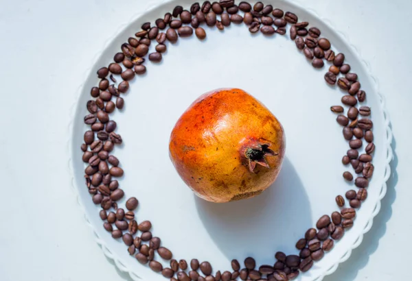 Coffee beans in round shape on the white plate with the pomegranate on the center