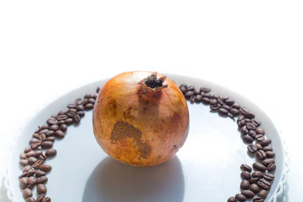 Kaffebönor i rund form på den vita plattan med granatäpple på center — Stockfoto