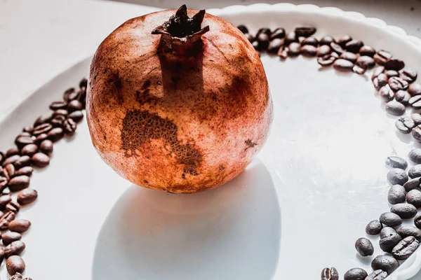 Coffee beans in round shape on the white plate with the pomegranate on the center