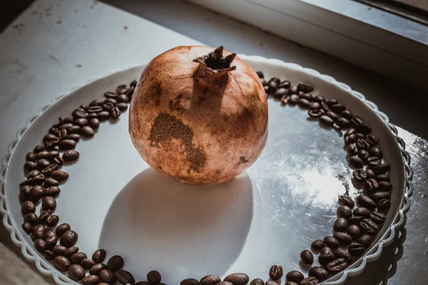 Biji kopi dalam bentuk bulat pada piring putih dengan delima di tengah — Stok Foto