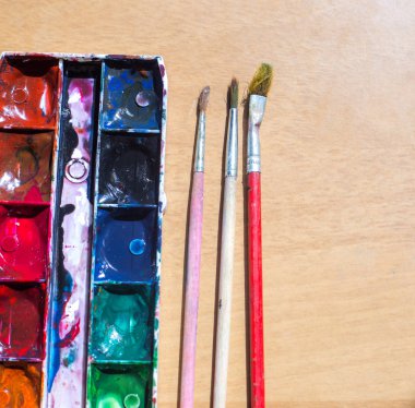 Ahşap masa üzerinde eski kullanılmış suluboya seti ve eski fırçalar