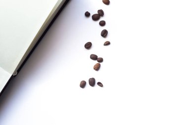Kahve çekirdekleri ve beyaz arka plan üzerinde açılan not defteri. Kopyalama alanı ile üstte görünüm