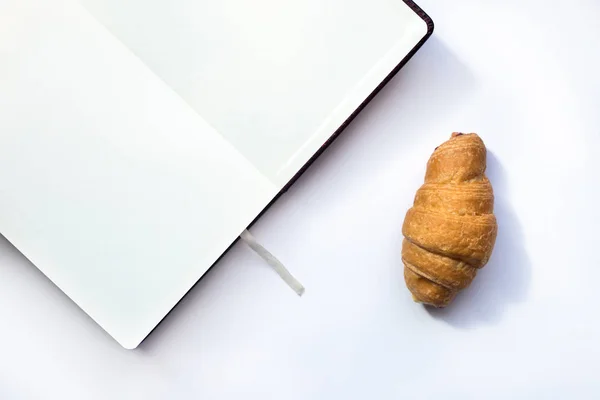 Croissant fresco y bloc de notas sobre fondo blanco. Vista superior con espacio de copia — Foto de Stock