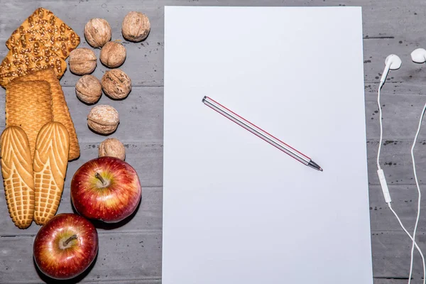 Galletas, nueces, manzanas, auriculares y papel a4 en blanco en el escritorio. Vista superior — Foto de Stock