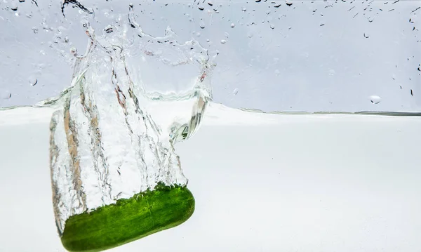 Groene komkommer gedaald in water geïsoleerd op wit — Stockfoto