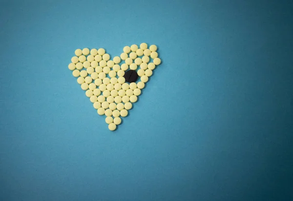 Yellow pills in shape of heart with the big black tablet — Stock Photo, Image