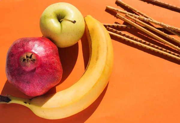 Золотое яблоко, свежий банан, гранат и соленые палочки — стоковое фото