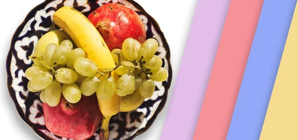 Fresh fruits placed on ornamental ceramic plate with multicolored stripes from right side — Stock Photo, Image