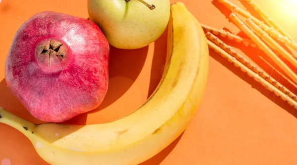 Золотое яблоко, свежий банан, гранат и соленые палочки — стоковое фото